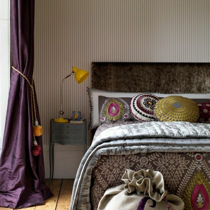 eklektische-Gestaltung-Schlafzimmer-Bett-Boho-Kissen-gelbe-Leselampe-lila-Satin-Gardinen-Quasten