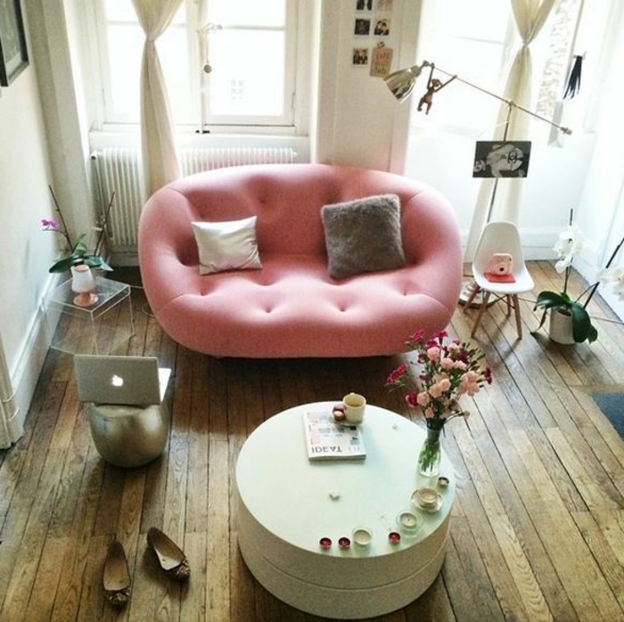 kleines-Zimmer-kokette-rosa-Couch-interessaante-Form-runder-Couchtisch-Blumen-Kerzen-Laptop