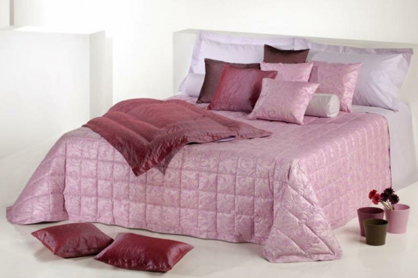 schlafzimmer mit einem bett mit rosigen und lila bettbezügen und kissen
