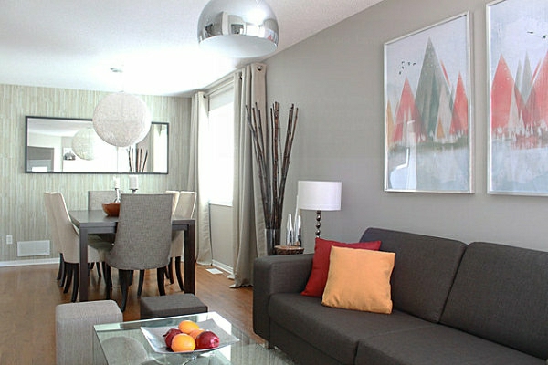 schöner-wohnen-farben-dunkles-sofa-mit-einem-orangen-dekokissen-und-grauer-wand-mit-bildern