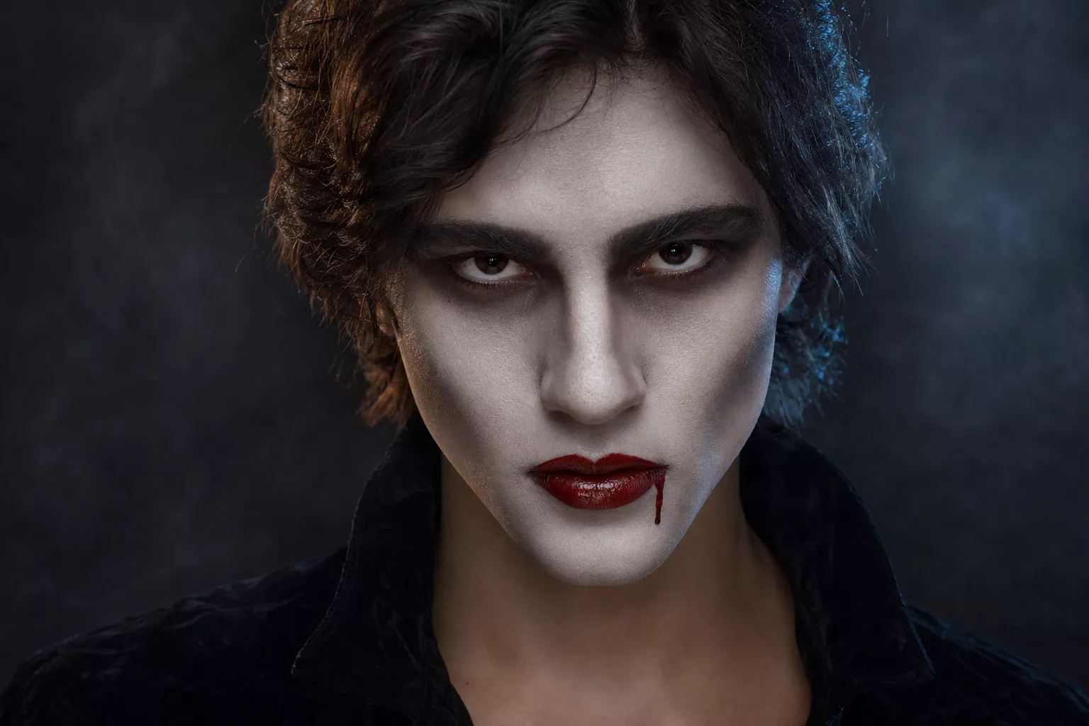 Vampirgesicht schminken: bleiche Haut, dunkle Augen, blutrote Lippen mit Blutstropfen