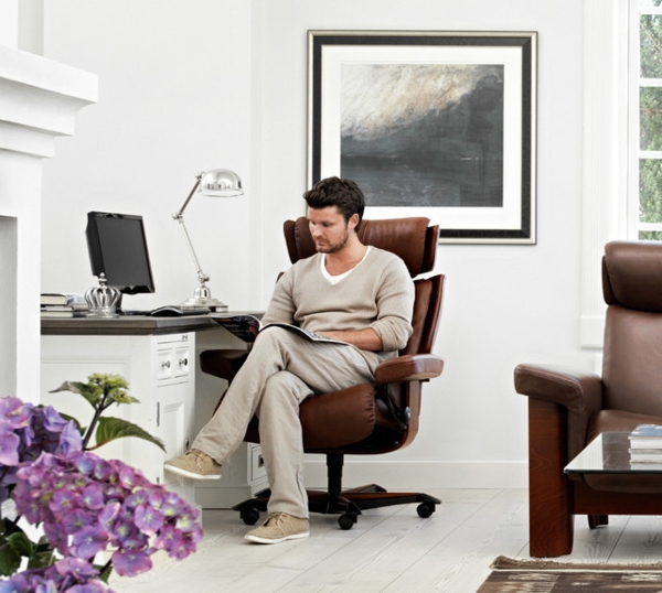 ein-mann-arbeitet-und-sitzt-auf-einem-stressless bürostuhl-ein großes bild dahinter