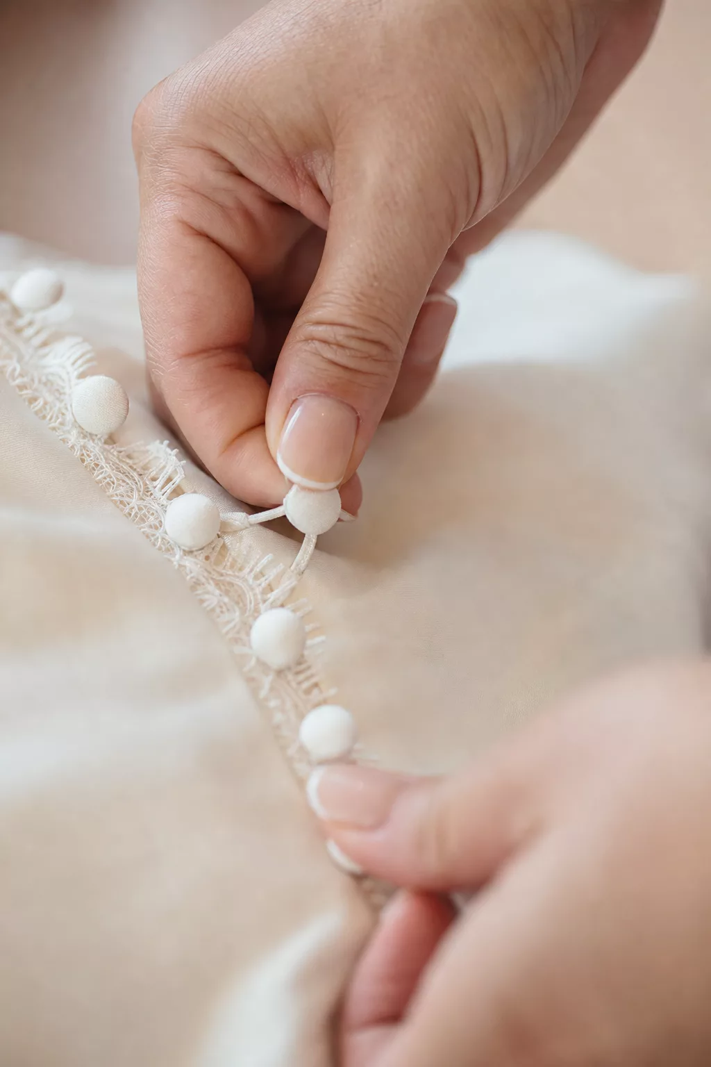 Hände schließen kleine Knöpfe am Rücken eines Brautkleids in Nahaufnahme