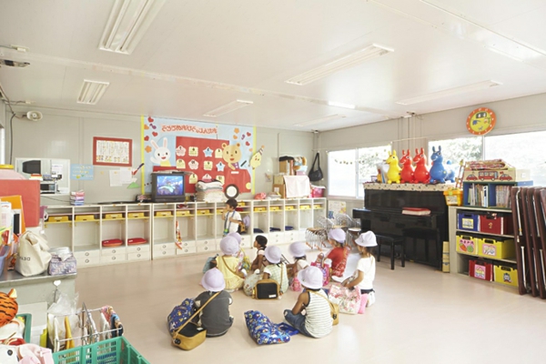 kindergarten-interieur-weiße-regale-im-zimmer-mit-vielen-auf-dem-boden-sitzenden-kindern