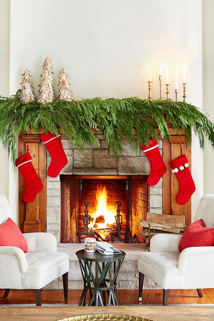 Kamin weihnachtlich dekorieren, grüne Zweige, vier rote Weihnachtsstrümpfe, Kerzen und kleine Weihnachtsbäume 