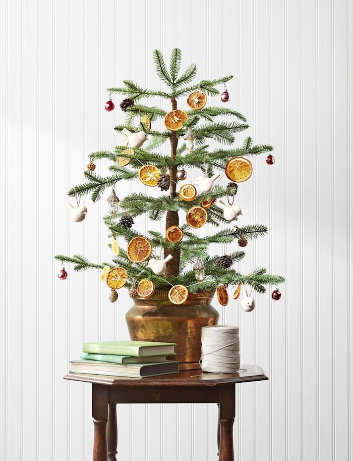 Kleiner echter Weihnachtsbaum in Blumentopf, geschmückt mit getrockneten Orangenscheiben, Tannenzapfen und Kugeln 