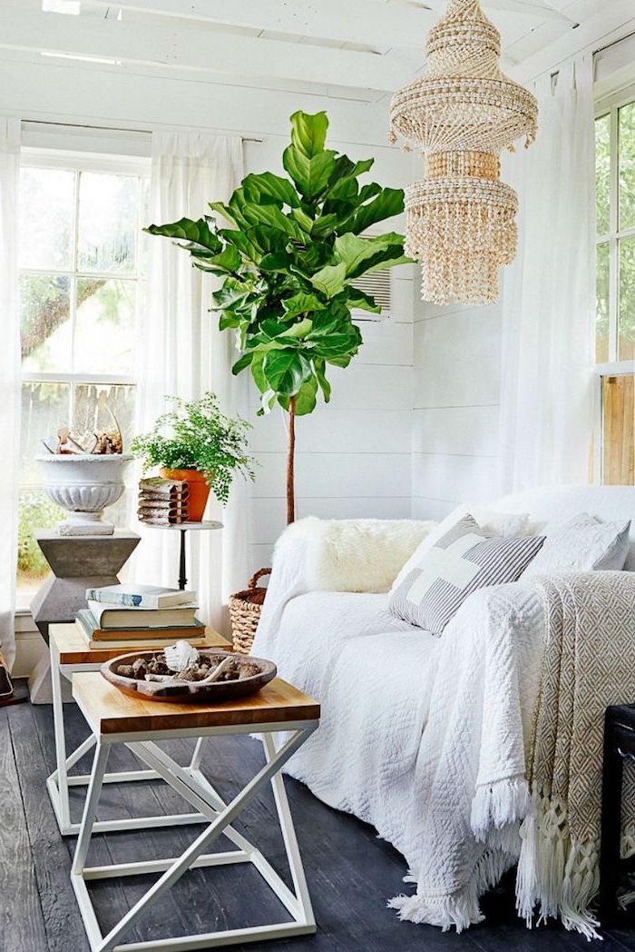 Wohnzimmer einrichten, weißer Sessel, viereckiger Couchtisch, verspielter Kronleuchter und große Grünpflanze 