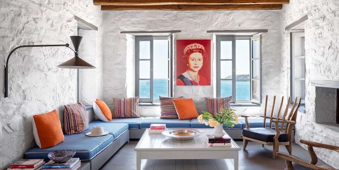Wohnzimmer in Greek Wohnstil, grobe Wände in Weiß, Queen Porträt, blaues Sofa mit bunten Kissen, viereckiger weißer Couchtisch 