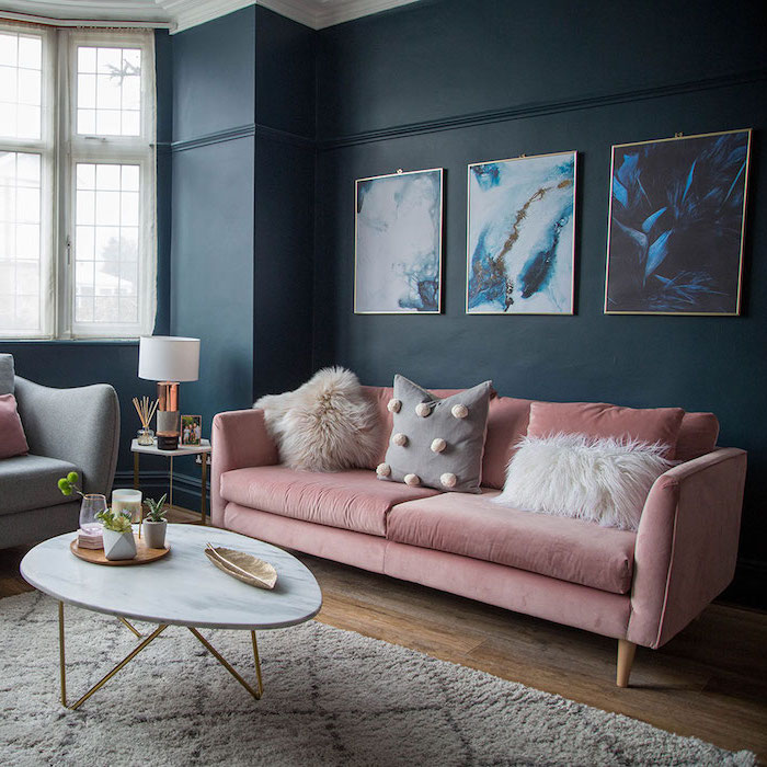 Wohnzimmer Einrichtung in Pastellfarben, rosafarbenes Sofa mit flauschigen Deko Kissen, Wandfarbe Dunkelblau, abstrakte Gemälde 