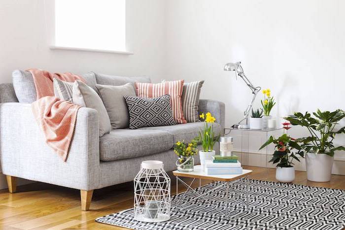 Wohnzimmer in Skandinavischer Stil einrichten, Wandfarbe Weiß, graues Sofa, viele Pflanzen, Narzissen in kleinen Blumentöpfen 