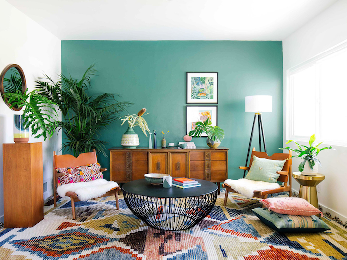 Vintage Wohnzimmer Einrichtung, eine Wand in Grün, Retro Möble aus Holz, bunter Teppich, runder Couchtisch, große Grünpflanzen 