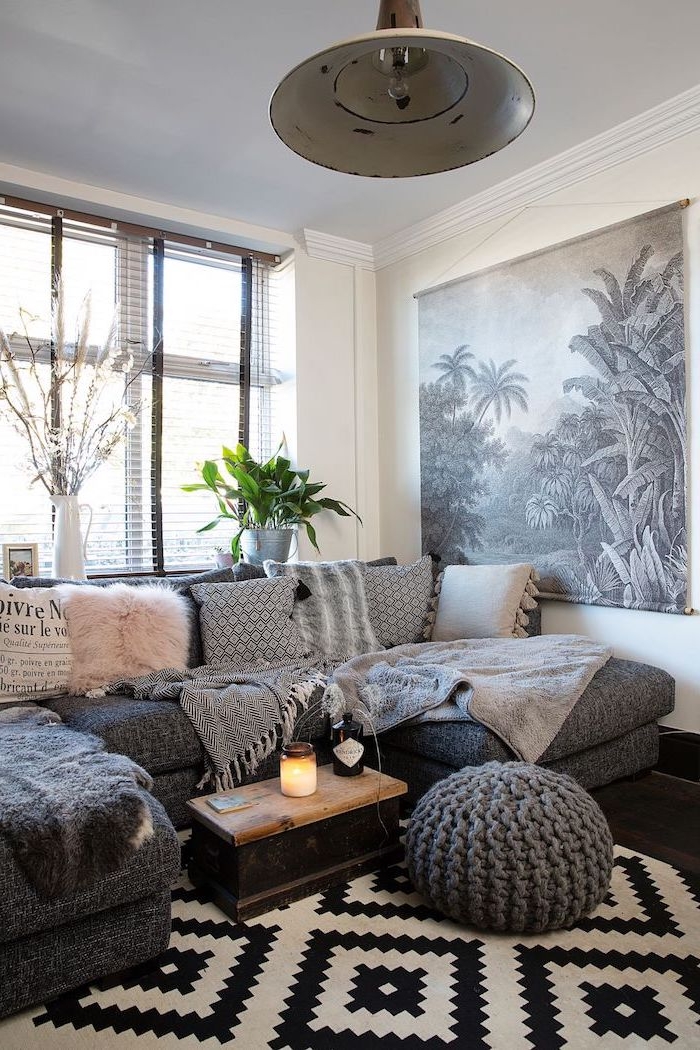 Boho Wohnzimmer Ideen, graues Sofa mit kleinen Deko Kissen, gestrickter Hocker, Teppich in Schwarz und Weiß 