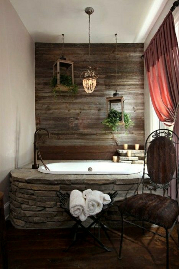Badezimmer-rustikales-Design-Badewanne-massive-Steine-hölzerne-Wand-Kerzen-rote-Gardinen-aristokratischer-Stuhl