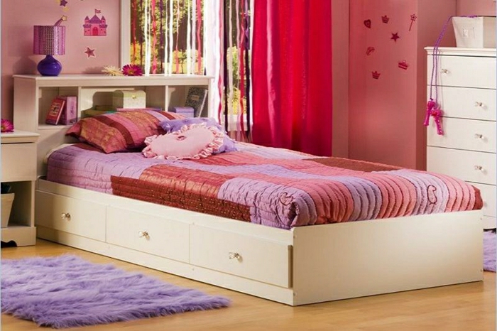 Kinderzimmer-rosige-Wände-flaumiger-Teppich-weißes-Bett-Schubladen-Bettwäsche-lila-rot-rosa-Kissen-Kommode-Spielzeuge