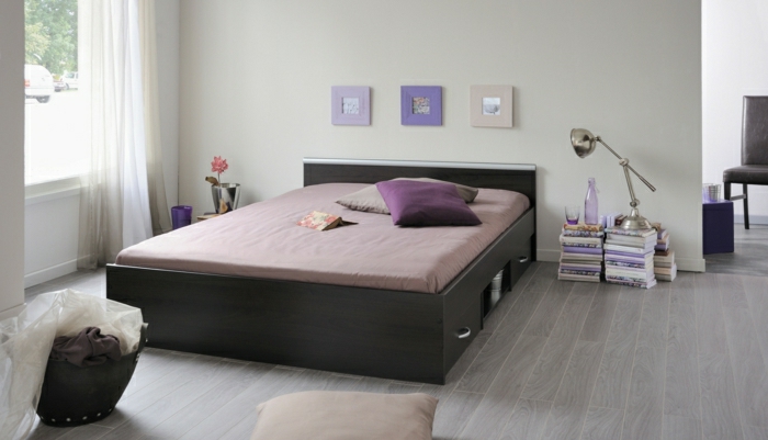 Schlafzimmer-breites-Bett-Schubladen-lila-Bettwäsche-Kissen-Bilder-Rahmen-lila-Nuancen-Bücher-Flasche-Glas-stilvoll