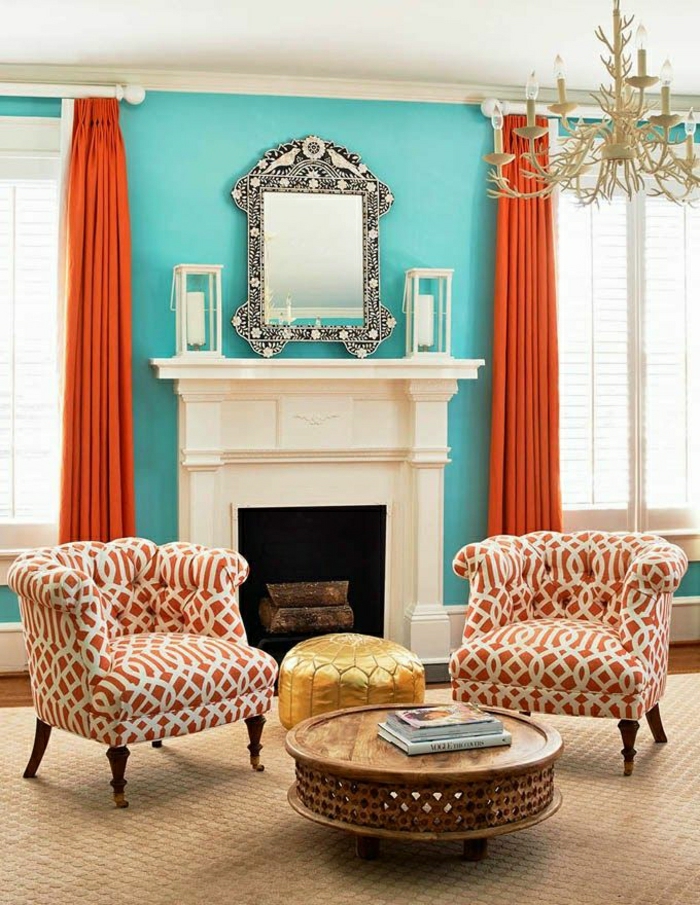 Wohnzimmer-eklektische-Gestaltung-Sessel-hölzerner-Couchtisch-Ornamente-goldener-Hocker-Kamin-blaue-Wönde-vintage-Spiegel-rustikaler-Kronleuchter-orange-Vorhänge-Rolladen