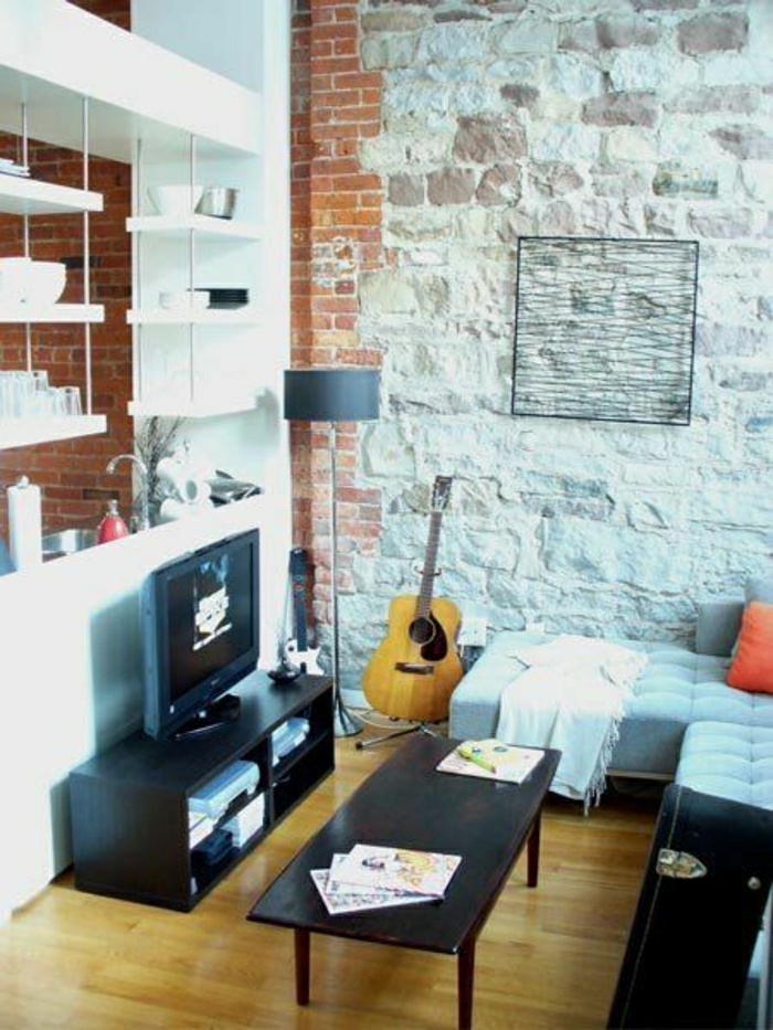 das-Musikinstrument-Gitarre-Wohnzimmer-Ziegelwände-Fernseher-weiße-Regale-Sofa-Kissen-Couchtisch