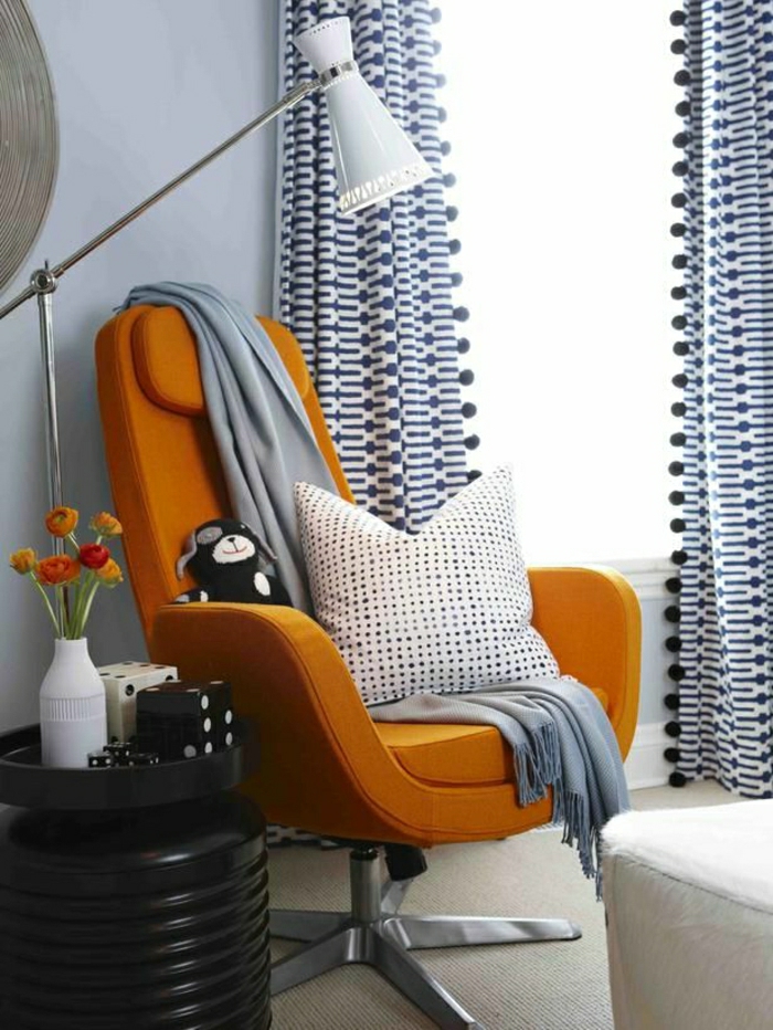 gemütliches-Wohnzimmer-orange-Sessel-graue-Schlafdecke-gepunktetes-Kissen-industrielle-Leselampe-Würfel-Plüschtier-moderne-Gardinen-blau-weiß