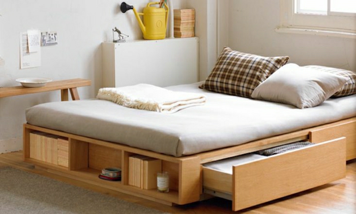 hölzernes-Bett-Schubladen-weiße-Wände-beige-Bettwäsche-Bücher-minimalistisch