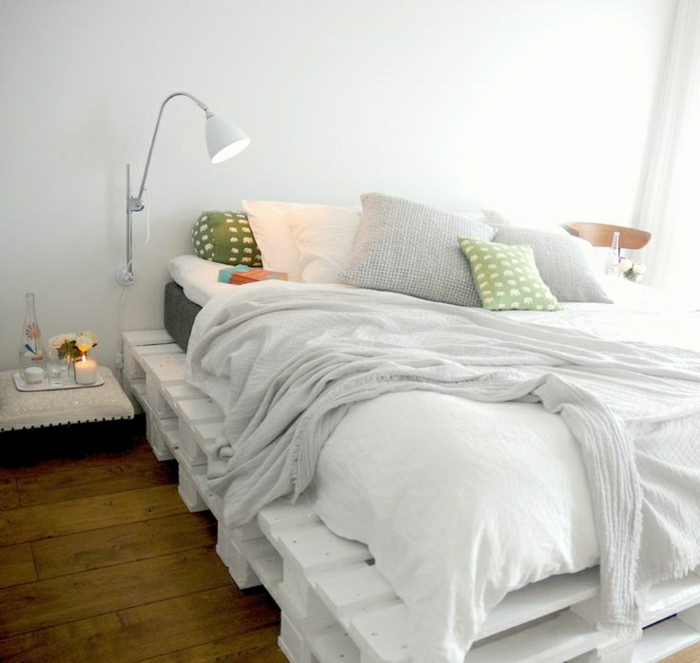 Bett-aus-Paletten-weiß-Kissen-lustiges-Muster-Leselampe-weiße-Bettwäsche