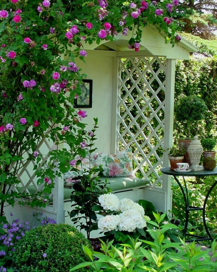 Gartenbank-mit-Dach-weiß-Dach-Gitterwände-Blumen-Kissen-Tisch-Blumentöpfe