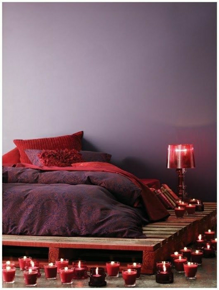 Schlafzimmer-attraktiv-lila-Bettwäsche-rote-Kissen-Kerzen-Nachttischlampe-Paletten-Rahmen-Bett
