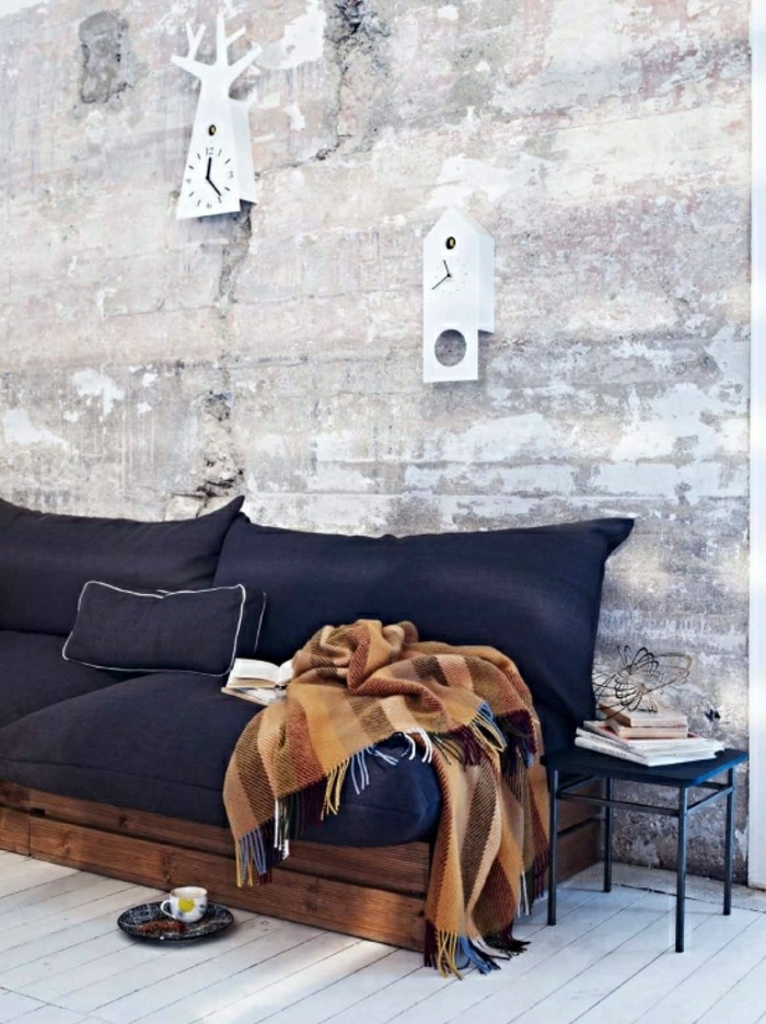 minimalistisches-Interieur-räumliches-Zimmer-Paletten-Couch-blaue-Polster-vintage-Schlafdecke-Wanduhren-Ziegelwände