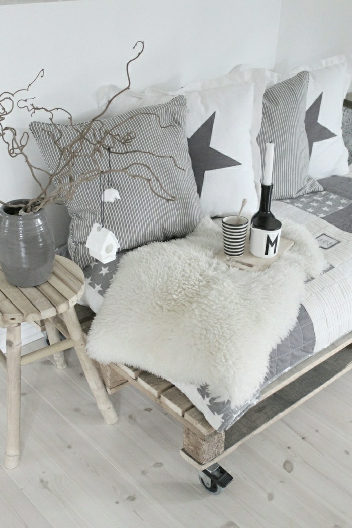 skandinavisches-Interieur-minimalistisch-weiß-grau-Sofa-aus-Paletten-Hocker-Tassen-Topf-Kissen