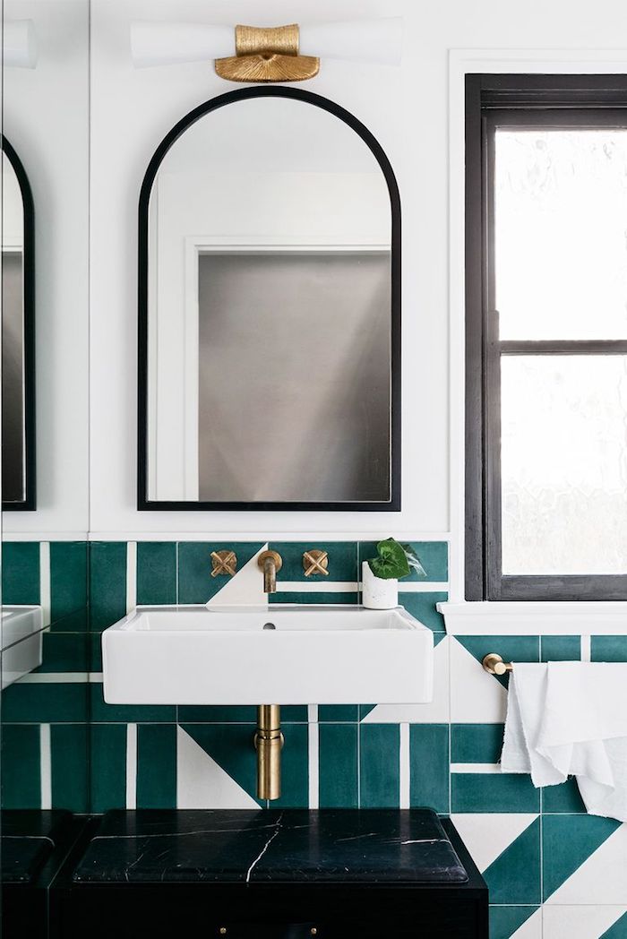 Abgerundeter Spiegel mit schwarzem Rahmen, grünblaue Fliesen und weißer Waschbecken 