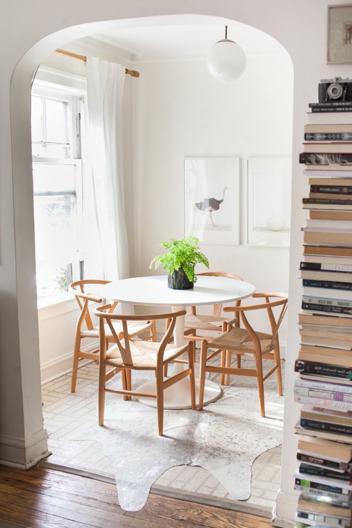gemütlich-eingerichtetes-Zimmer-weißer-Tisch-hölzerne-Stühle-einfaches-Design-Pflanze-Bücher-Kolonne