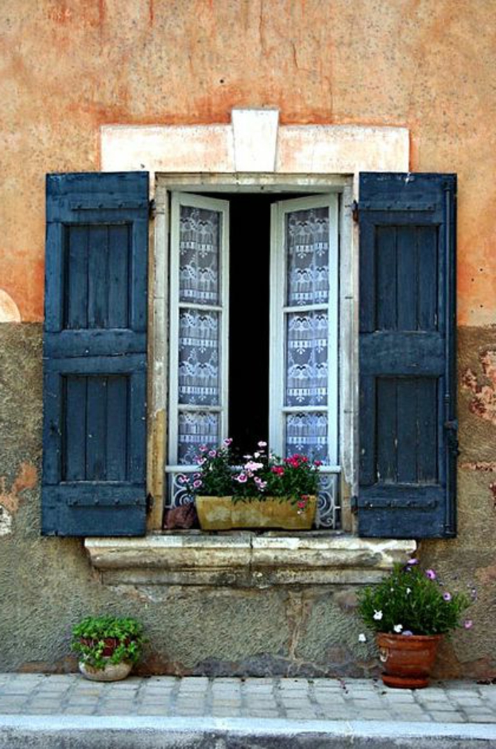 Straße-altes-Gebäude-Fenster-schöne-Gardinen-dunkelblaue-Läden-Blumentöpfe