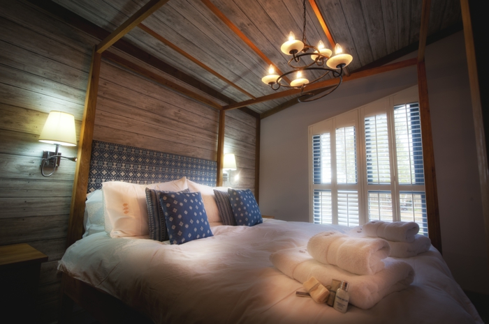 elegantes-Schlafzimmer-stilvoller-Kronleuchter-großes-Bett-blaue-Kissen-Tücher-landhausstil