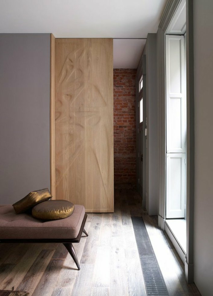 kreative-Schlafzimmer-Gestaltung-hölzerne-Tür-Ziegelwand-brauner-Liegestuhl-goldene-Kissen