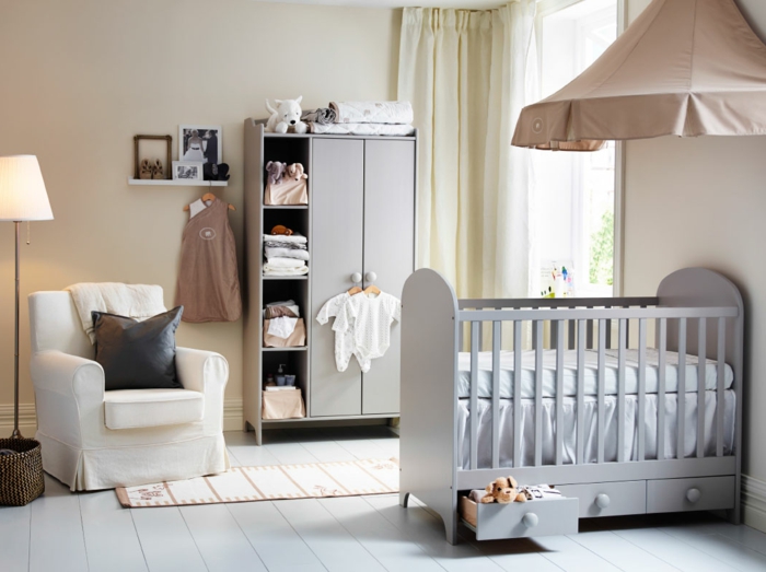 stilvolles-Kinderzimmer-Interieur-grau-braun-Babybett-Schirm-Kleiderschrank-Babykleider-Regal-Fotos-Sessel-Creme-Farbe-schwarzes-Kissen