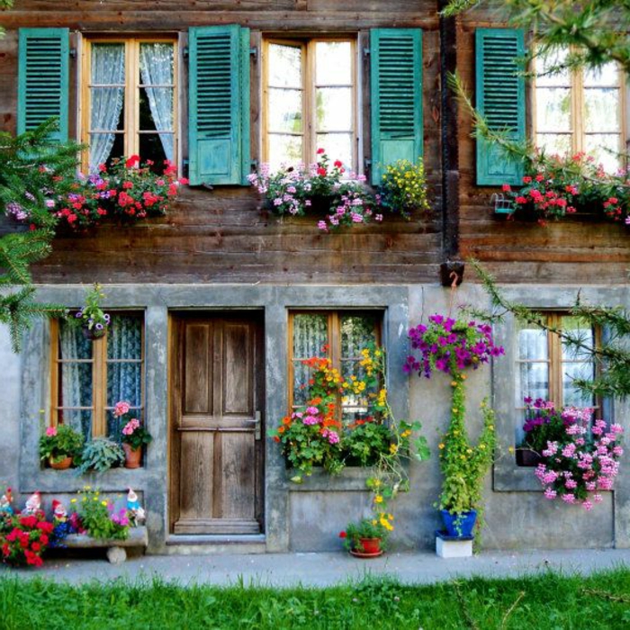 zweistöckiges-Haus-Schweizer-Alpen-Fenster-bunte-Läden-viele-Blumen-romantisch-gemütlich