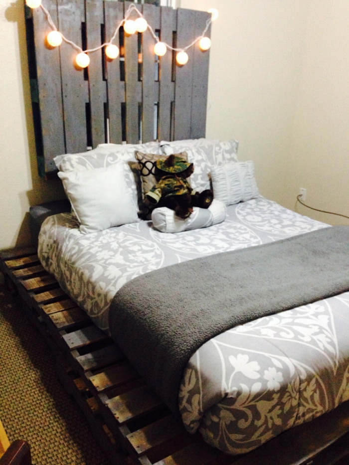 Kopfbrett-Bett-aus-paletten-hängende-Glühbirnen-schlichtes-Schlafzimmer-Interieur-graue-Schlafdecke