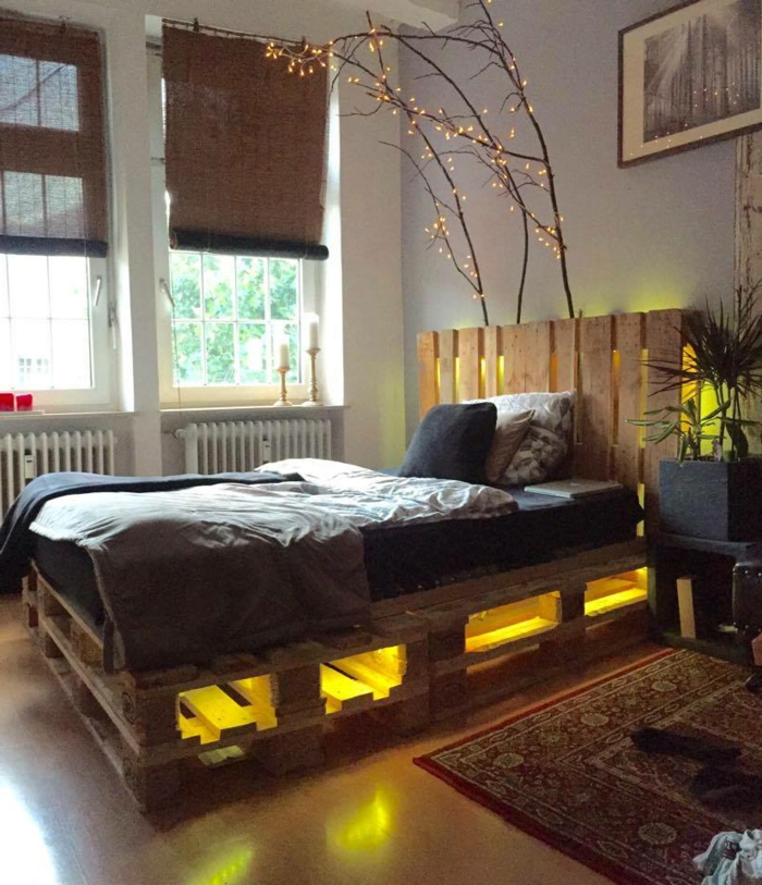 Schlafzimmer-schlichtes-Interieur-bett-aus-europaletten-innere-Beleuchtung-gelbes-Licht-dekorative-Zweige