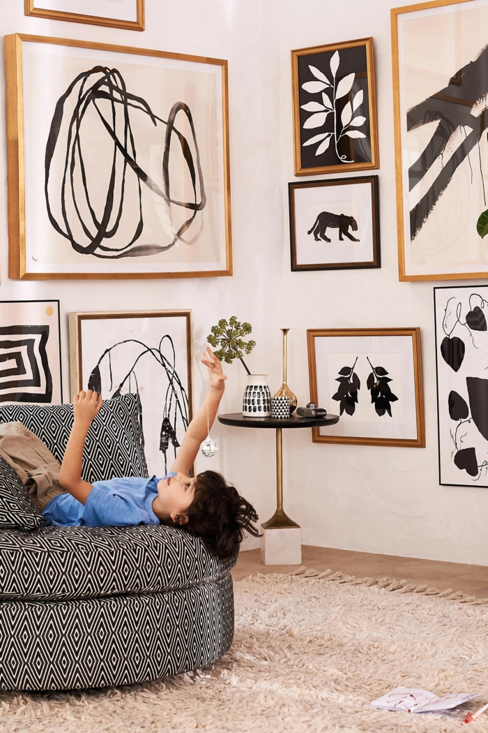 Wand dekoriert mit verschiedenen Bildern, Bilder mit Rahmen, Kind im blauen Hemd auf Sofa. Schwarz-weiße Zeichnungen