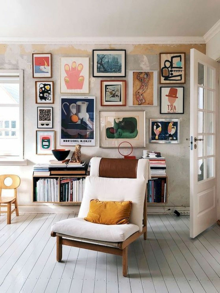 Bunte Bilder artistisch gestaltet auf Wand, gemalte Bilder, Sessel aus Holz mit weißem Kissen, kleiner Stuhl in gelb, kleine Kommode mit Magazine