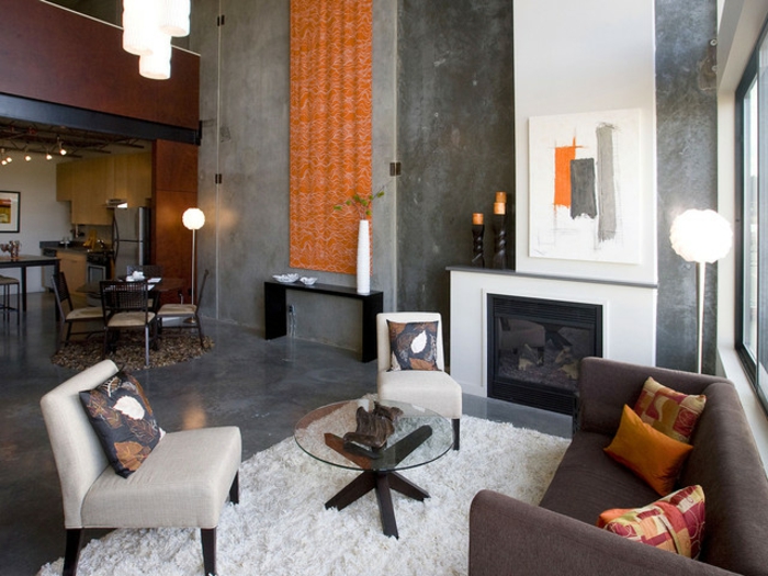 gemütliches-Wohnzimmer-raues-Interieur-Beton-Marmor-graue-Nuancen-Kamin-orange-Akzente-Teppich-weiß
