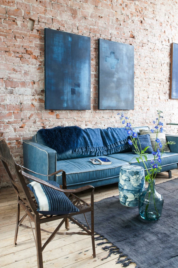 Zwei blaue Gemälde aufgehängt an Ziegelwand, großer Sessel und Teppich in blau, Stuhl aus Holz, außergewöhnliche Bilder