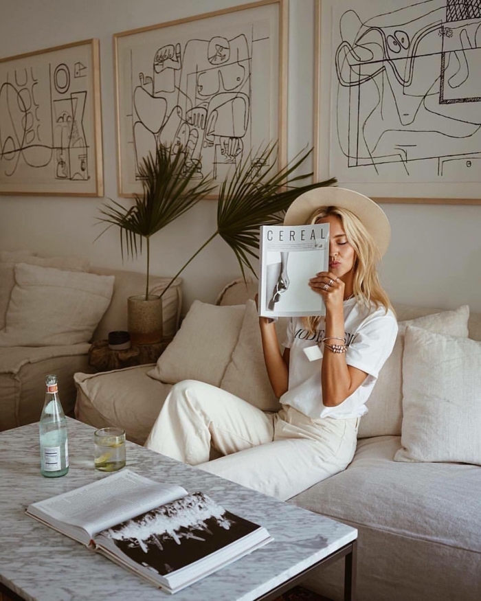 Drei große Linienzeichnungen, Bilder mit Rahmen, Blonde Frau in weißem Outfit liest Magazin auf weißem Sofa