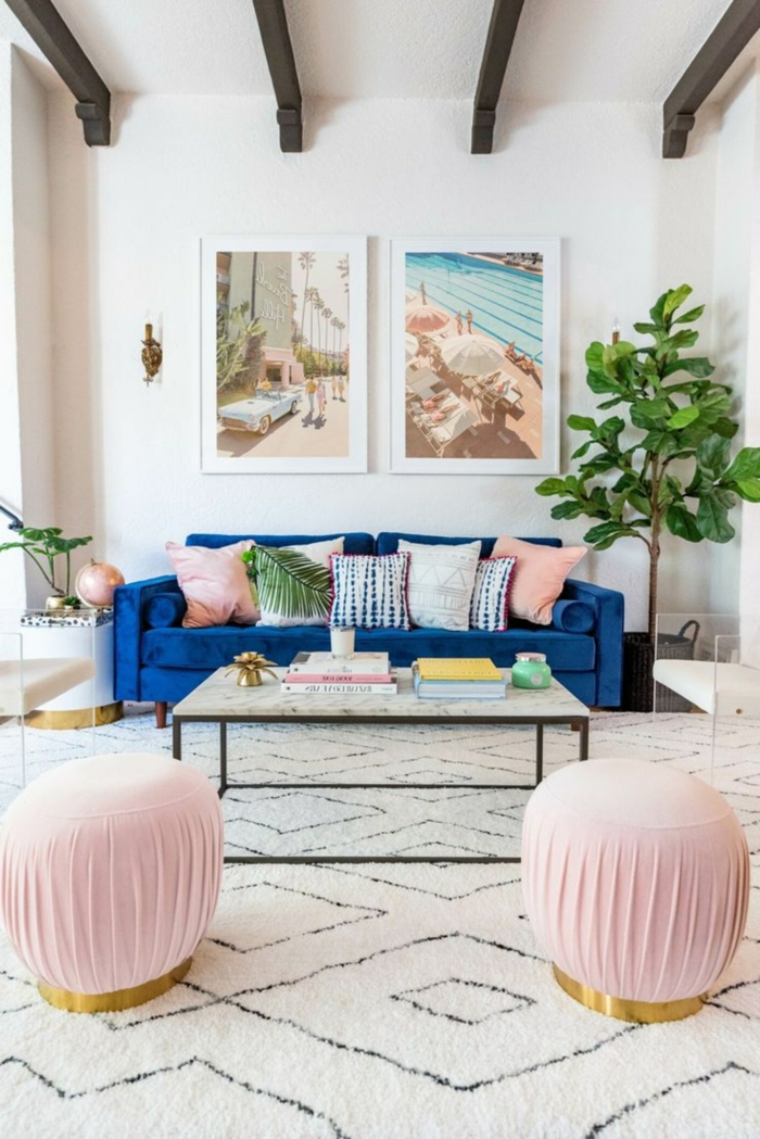 Couch in Blau mit vielen Kissen, rechteckiger Tisch, zwei kleine Hocker in pink, gerahmte Bilder für Wohnzimmer