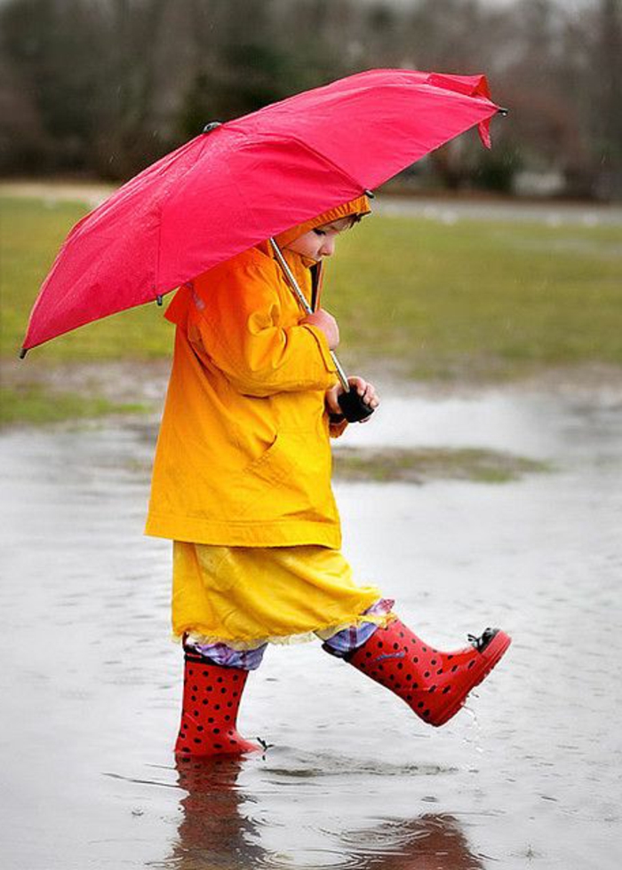 süßes-Kind-roter-Kinder-Regenschirm-im-Regen-laufen