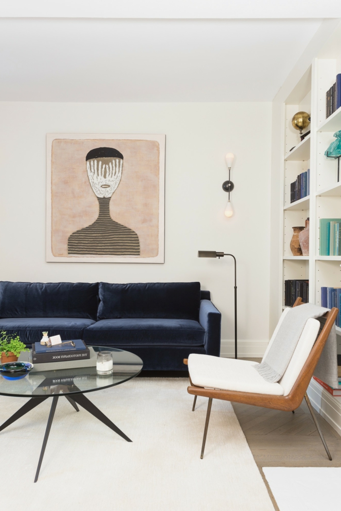 Großes Regal mit Büchern, Große Wandbilder von abstrakte Kunst, Bild von einem Gesicht, Sofa in blau, Teppich in weiß, runder Tisch
