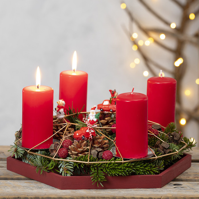 Adventskranz mit vier roten Kerzen, dekoriert mit Tannenzweigen, kleinen Weihnachtsfiguren und Zapfen 