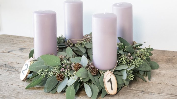 DIY Adventskranz, vier lila Kerzen, grüne Blätter und Schilder mit Nummern von 1 bis 4