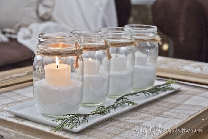 Vier Einmachgläser voll mit künstlichem Schnee, vier weiße Kerzen darin, DIY Adventskranz Idee