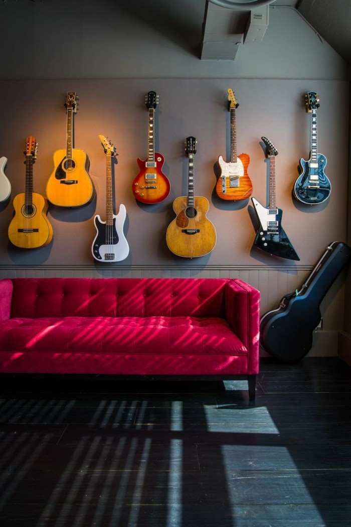 artistisches-Interieur-viele-Gitarren-hängend-an-der-Wand-schlichtes-Modell-rote-Couch