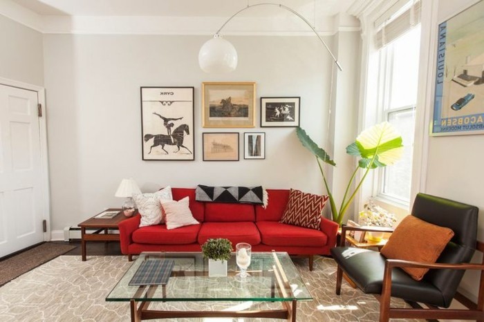schlichtes-Interieur-weiße-Wände-Topfpflanze-Designer-Leuchte-schwarzer-Ledersessel-rote-Couch-gläserner-Kaffeetisch